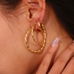 Macro shot of twisted gold hoop earrings set showing triple stack on earlobe