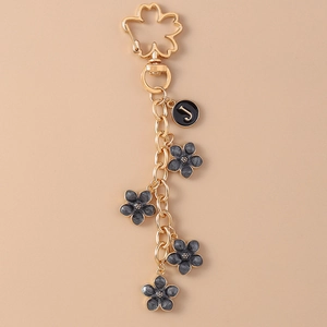 Detailed close-up of golden daisy keychain with letter J pendant and dark grey flower charms