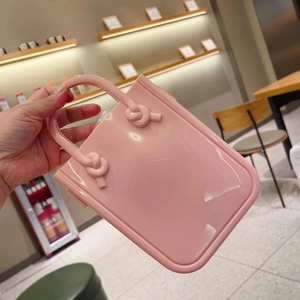 Detailed view of pink jelly PVC handbag with knotted handles held in a bright setting