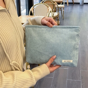 Detail of light blue corduroy cosmetic bag with brand tag held in a cafe setting
