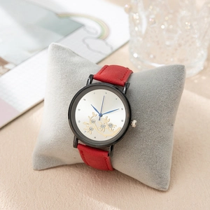Détail d'une montre à bracelet rouge avec cadran fleuri doré sur un coussin gris