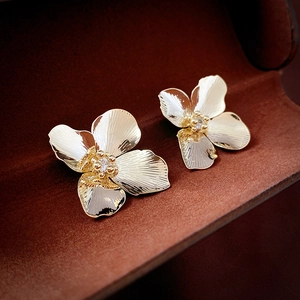 Close-up of golden flower stud earrings with zircon center on brown velvet