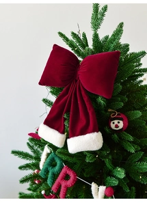 Close-up of a large red velvet Christmas bow with white fur trim on a tree top