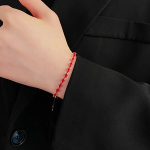 Close-up of a gold chain bracelet with red teardrop gem worn on a wrist against black suit