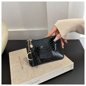 Detail of glossy black crocodile pattern mini pouch with gold zipper and tassel accessory