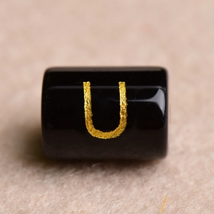 Macro shot of a polished black round bead with a golden engraved letter U for DIY jewelry
