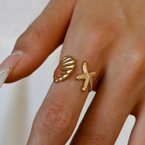Detail of gold starfish and shell open cuff bracelet on female wrist in vacation style