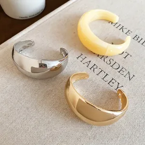 Bracelets joncs épais en forme de C en or, argent et crème sur une surface textile fine