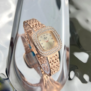 Macro shot of rose gold square watch with double diamond-encrusted bezel on reflective surface