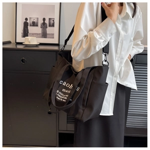 Detail view of large black canvas tote bag with white lettering and functional side pocket