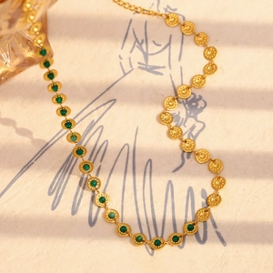 Detailed view of 18K gold plated necklace with green round stones on artistic paper