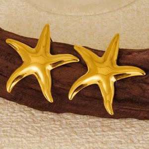 Macro shot of 18k gold starfish stud earrings on dark wood base with clear metal texture