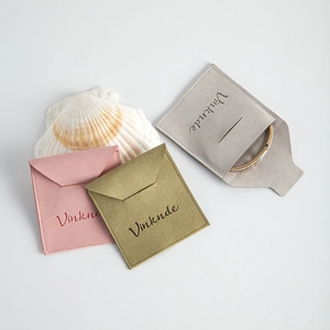 Primer plano de bolsas de microfibra para joyas en rosa, verde y gris con un brazalete