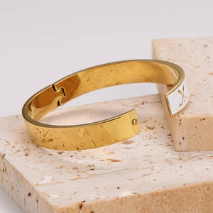 Luxury golf club style gold open bangle with white enamel inlay on stone pedestal