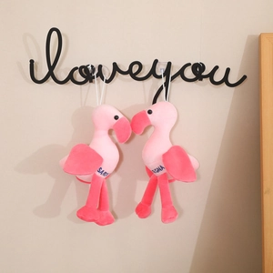 Pink plush flamingo toy set with heart embroidery hanging on a wall hook