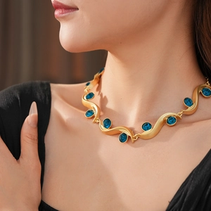 Close-up of golden wavy necklace with blue oval gemstone worn by a model