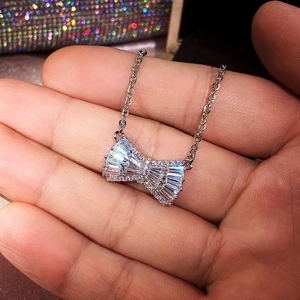 Macro detail of a silver bow necklace with sparkling zircon resting on a hand