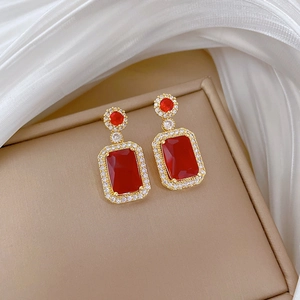 Macro shot of gold-plated earrings with rectangular red gemstones and white zircon halo