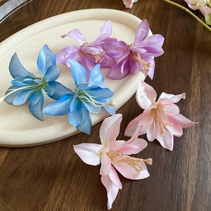 Detailed view of silk hibiscus flower hair clips in light blue, purple, and pink colors