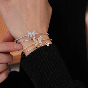 Close-up of stacked gold and silver butterfly bracelets with zircon on a female wrist