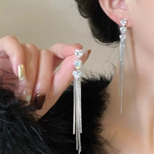 Detailed macro view of heart-shaped crystal studs and flowing silver fringe tassel earrings