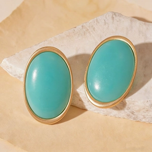 Close-up of vintage gold frame earrings with turquoise oval resin stones on white stone