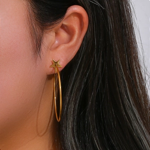 Detailed close-up of a golden star stud earring with a large circular hoop on a model