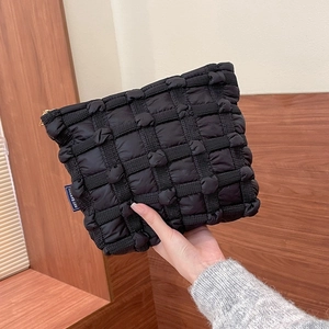 Close-up of black puffed quilted texture and woven label on a stylish makeup bag