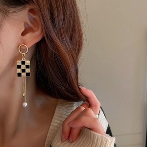 Detail of gold dangle earring featuring a checkered square pendant and a dangling pearl drop