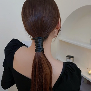 Detail of a black faux leather hair tie with gold metal tips on a ponytail hairstyle