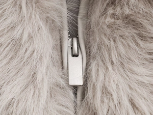 Detailopname van een zilveren metalen rits op een beige jas van imitatiebont