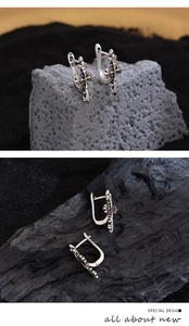 Close-up of vintage silver cross earrings with floral motifs on dark volcanic stone base
