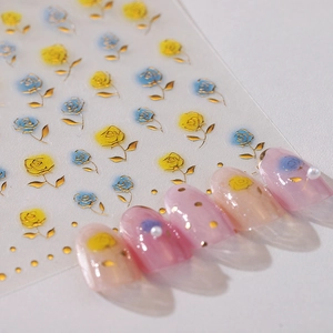 Stickers ongles 3D dorés avec motifs roses jaunes et bleues sur fond blanc