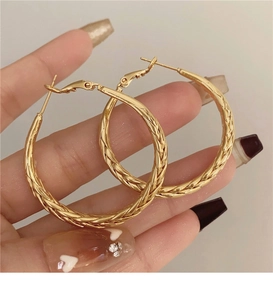 Detailed view of large golden twisted hoop earrings featuring intricate woven textures