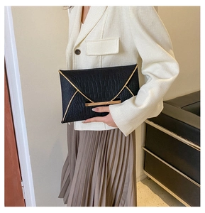 Détail d'une pochette enveloppe noire à motif crocodile avec bordure en métal doré