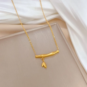 Detailed view of a gold bamboo-shaped pendant necklace with a leaf charm on silk fabric