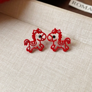 Close-up of red pony stud earrings with pearl accents on a textured beige surface