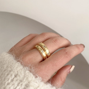 Primer plano de anillos apilables de latón dorado con circonitas en el dedo del modelo