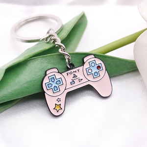 Close-up of a pink game controller enamel keychain with silver chain on white fabric