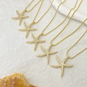 Macro detail of five gold starfish pendants with sparkling zircons on white paper
