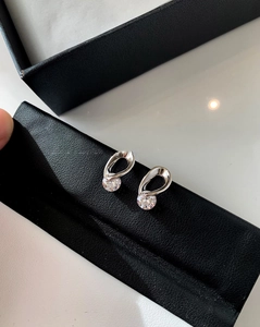 Detailed macro shot of silver hollow teardrop earrings with central zircon stone on leather
