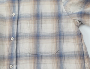 Dettaglio di camicia a quadri blu e beige con taschino sul petto e bottoni bianchi