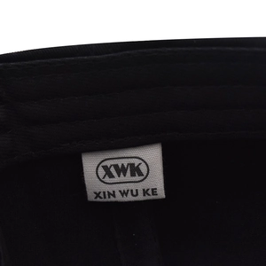 Close-up of the internal white woven label with brand logo on a black cotton baseball cap