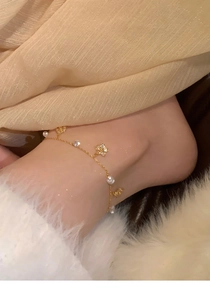 Detailed close-up of a gold clover anklet with zircon beads on a soft white background