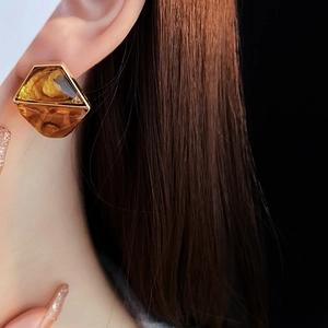 Close-up of geometric amber resin earrings with gold metal frame worn by a model