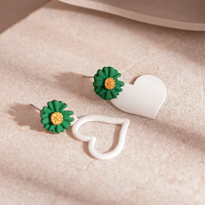 Macro shot of asymmetrical acrylic earrings featuring white hearts and green daisies