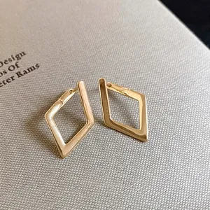 Minimalist geometric rhombic gold earrings with polished finish on gray fabric background