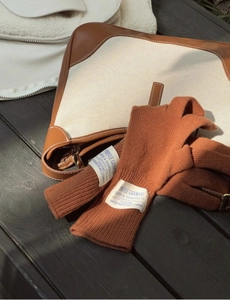 Detalle de guantes de punto naranja con etiqueta de tela vintage sobre madera