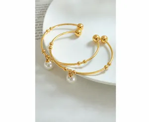 Detail of gold open bracelets featuring round ball ends and a white pearl charm on a ceramic tray