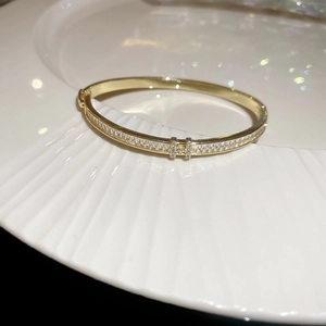 Macro detail of 18k gold plated bangle featuring a crystal-encrusted H-shaped centerpiece